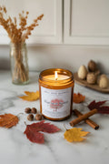 Burning amber glass Harvest Spice candle with exposed flame, surrounded by fall leaves