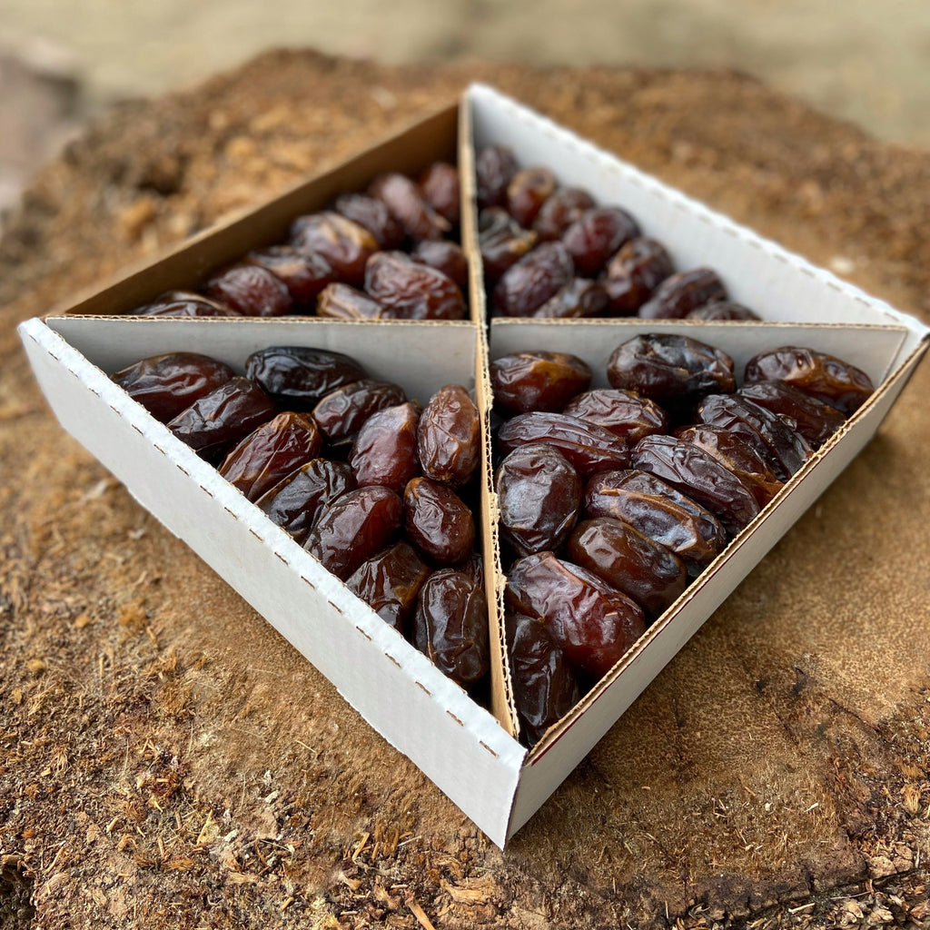 Soft Medjool dates packed in a split cardboard box, dark red dates visible