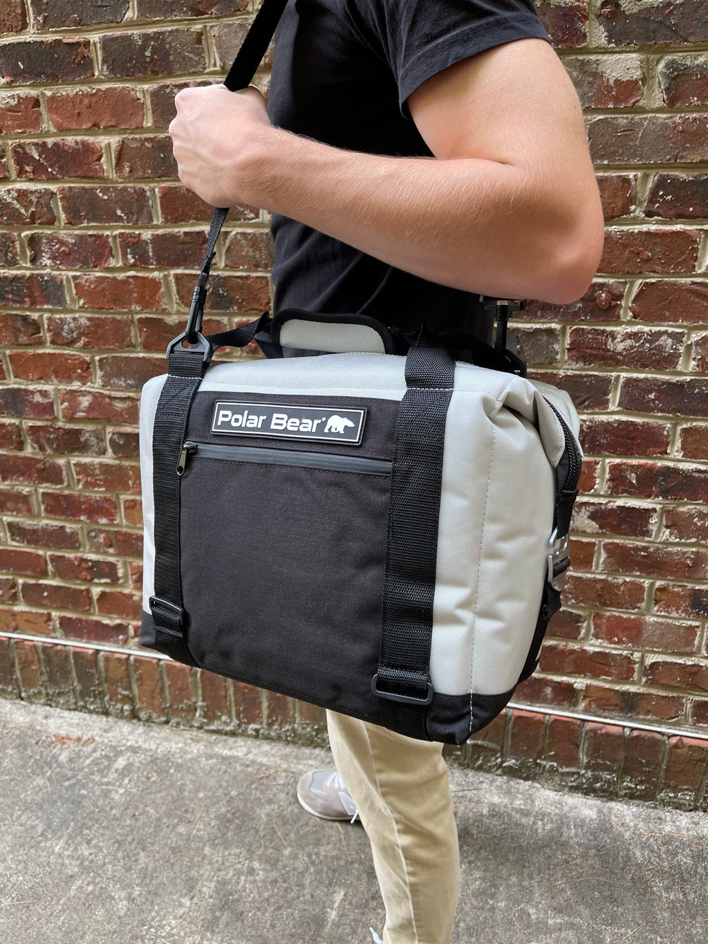 Soft cooler bag held by a person; black and light-colored panels with front logo