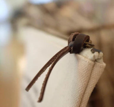 Beige canvas zip pouch with brown leather cord zipper pull and quote text.