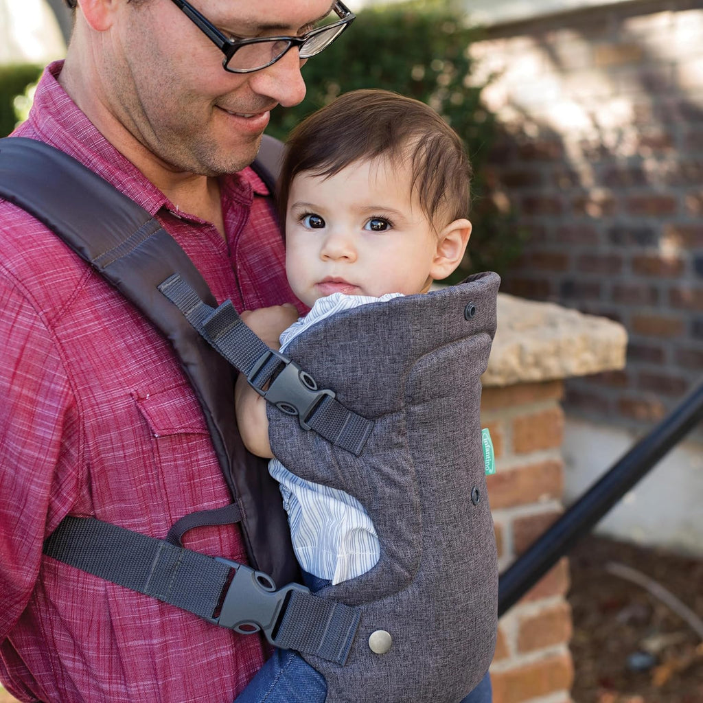 Gray convertible baby carrier worn front by parent; structured seat and adjustable harness straps