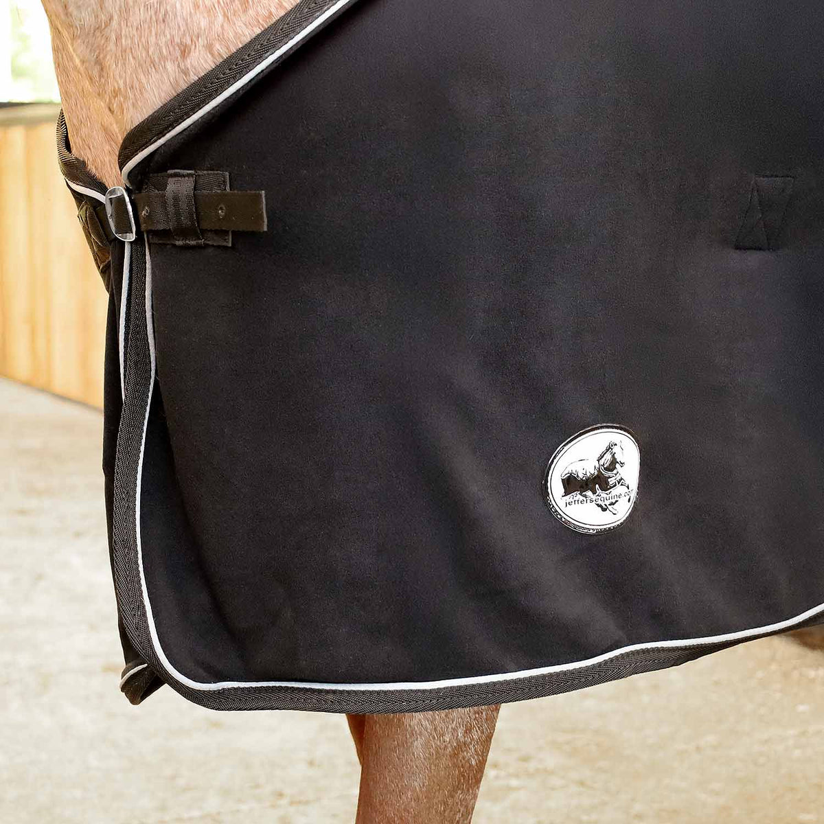 Black fleece horse cooler blanket side view with hanging tie and round logo patch