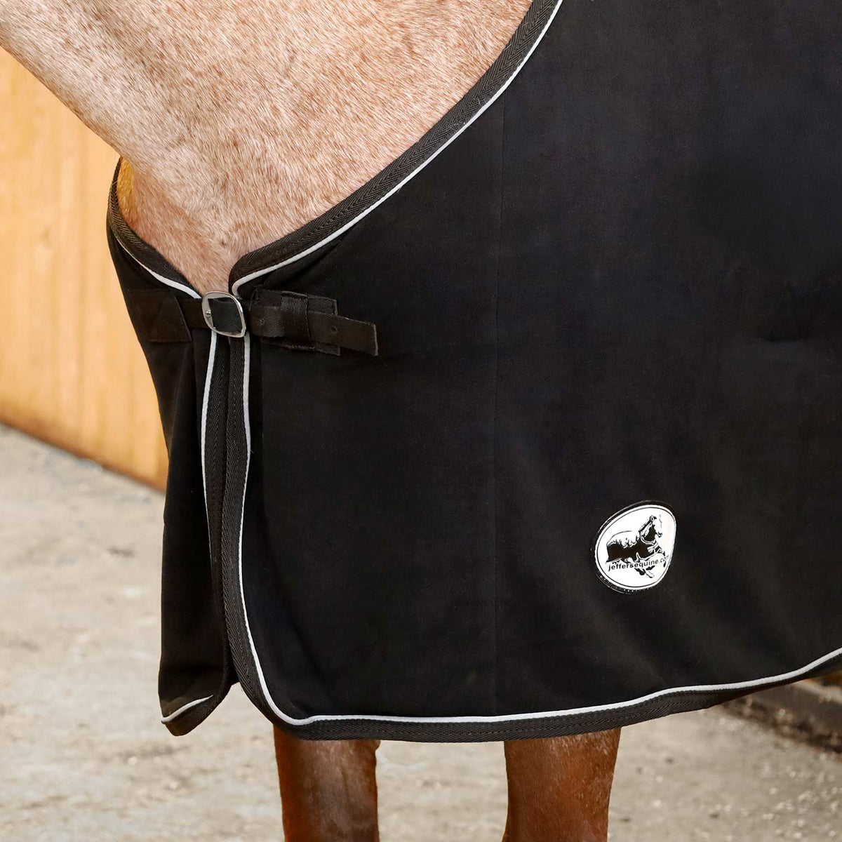 Black fleece horse cooler blanket close-up, front tie straps, white piping, logo badge