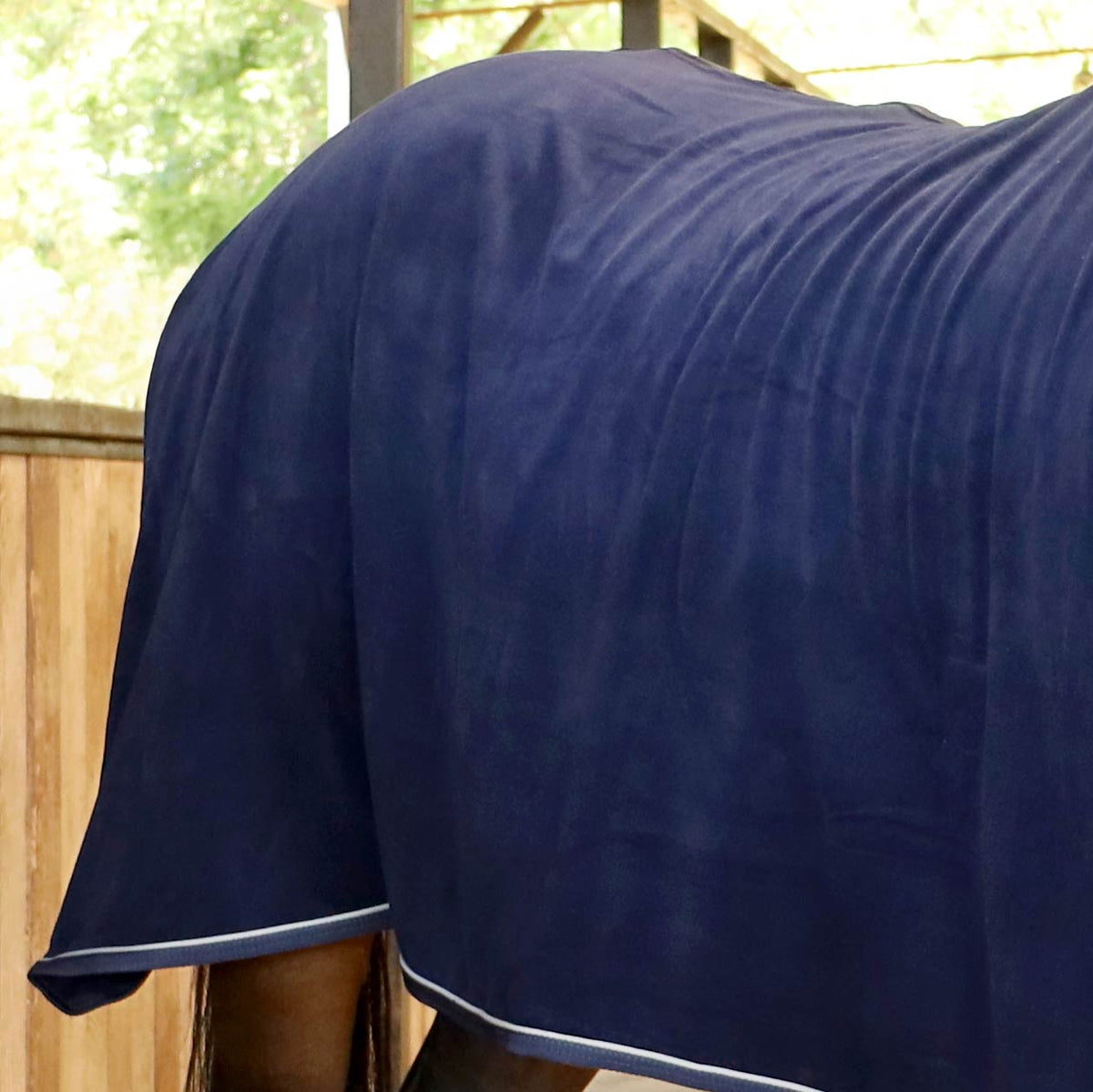 Navy fleece horse cooler blanket back view with white trim along hem