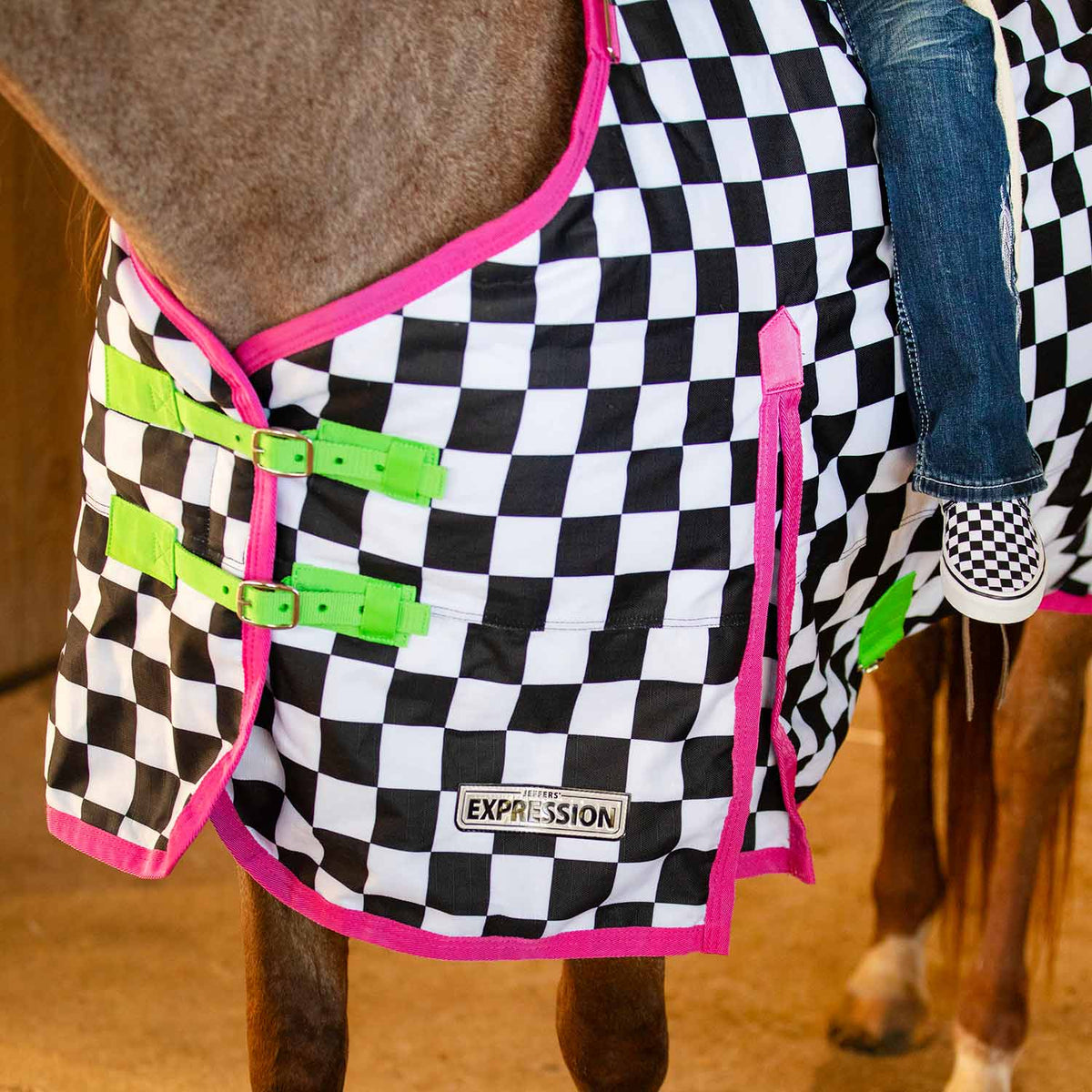 Black-and-white checkered turnout horse blanket with pink trim and green front belly straps