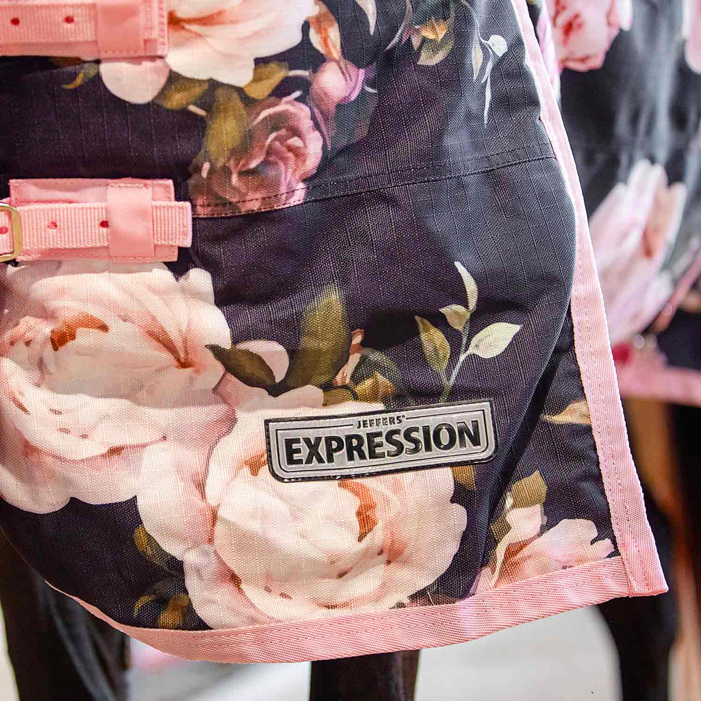 Horse turnout blanket close-up: dark fabric with pink floral print and Expression logo