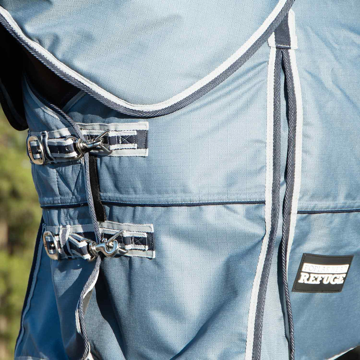 Light blue turnout blanket close-up of front buckles and adjustable chest straps