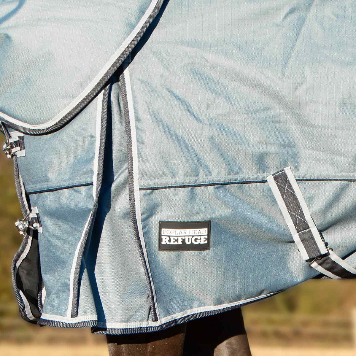 Light blue turnout blanket with Refuge chest patch and detachable neck strap, cropped view