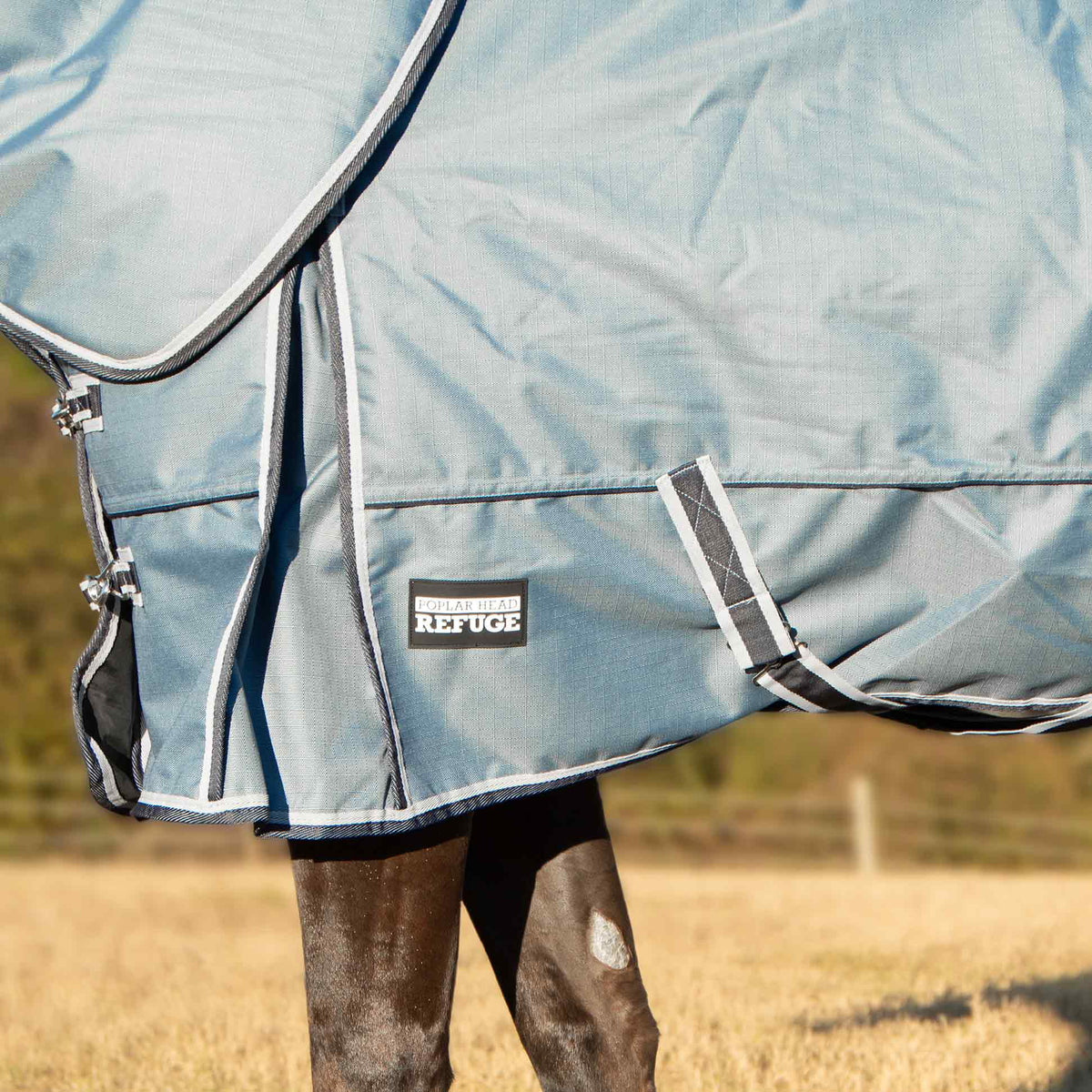 Light blue turnout blanket with Refuge chest patch and detachable neck strap close-up