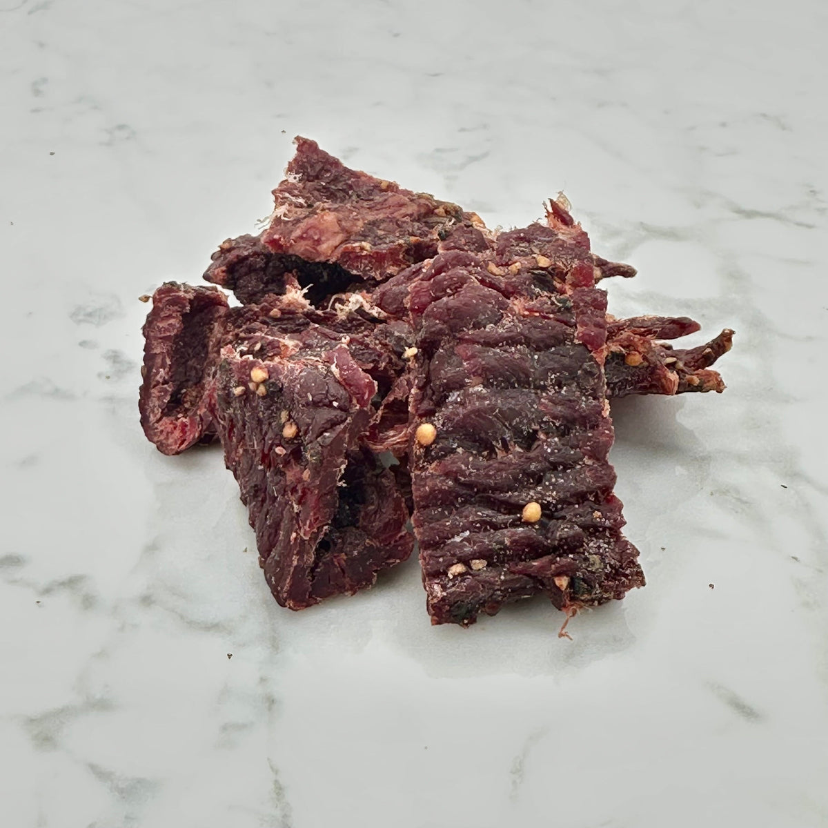 Dark red beef jerky strips, broken pieces in a pile