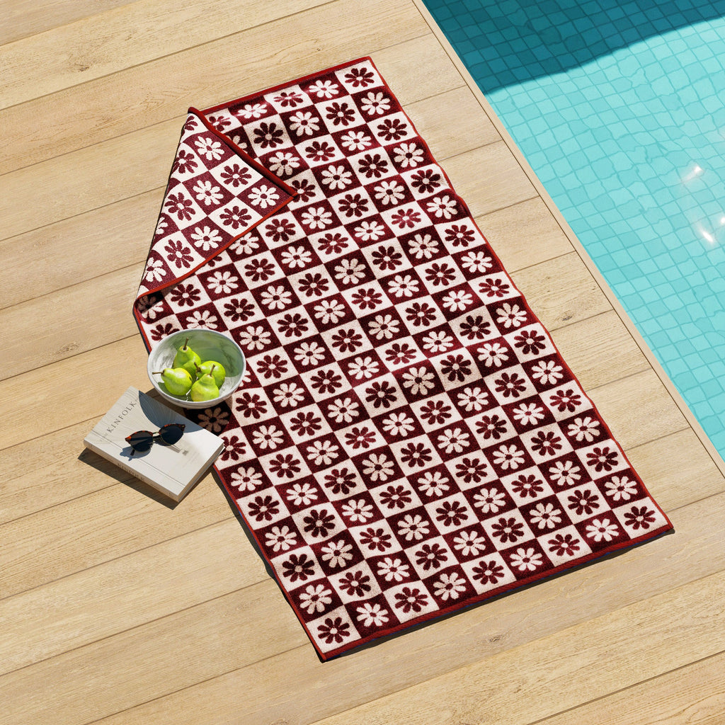 Cotton velour beach towel with red and white daisy-style flower pattern, folded.