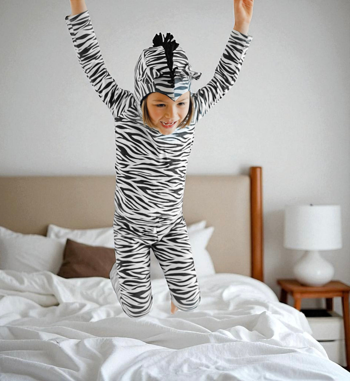 Kids zebra-print jumpsuit with long sleeves and headband, arms raised on bed