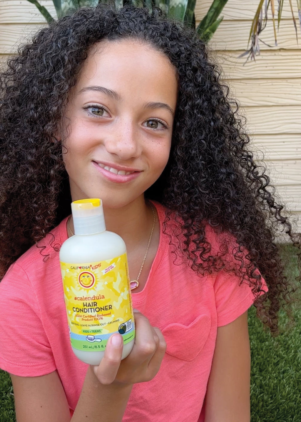 Kids Calendula hair conditioner bottle held by smiling child, yellow label, white cap