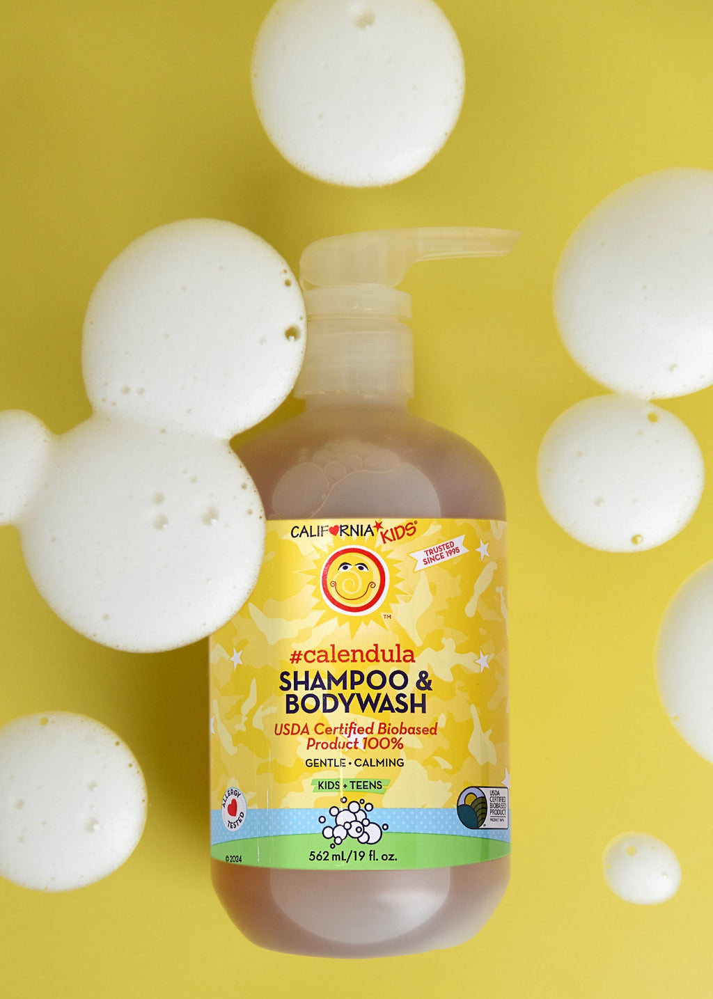 Kids Calendula shampoo & body wash bottle with yellow label, surrounded by white bubbles