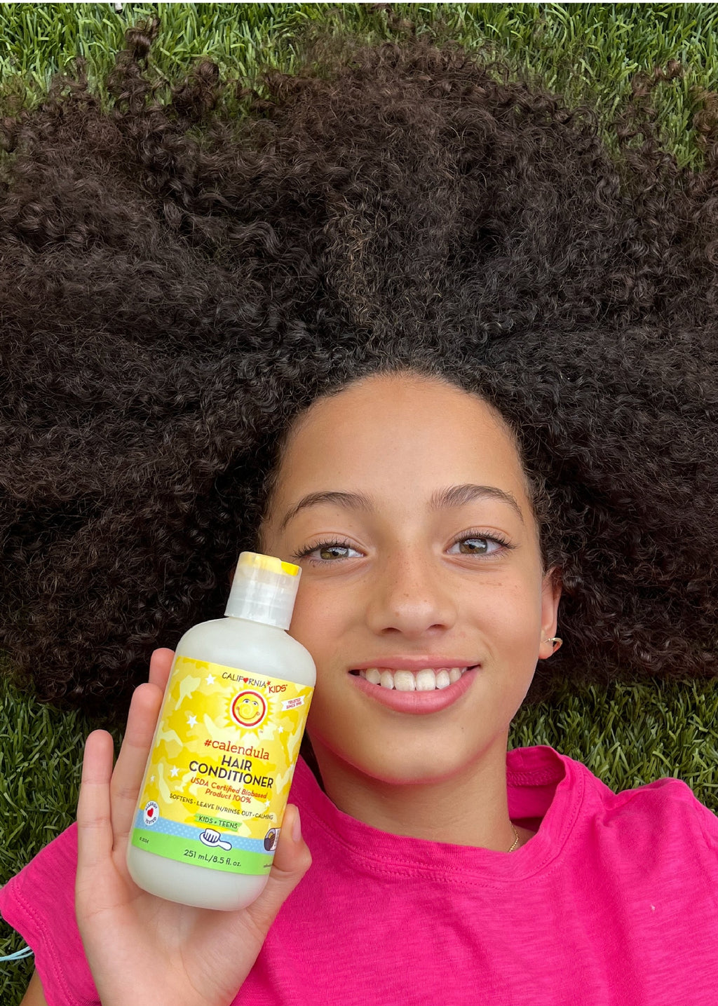 Kids Calendula hair conditioner bottle held near face, yellow label, white cap