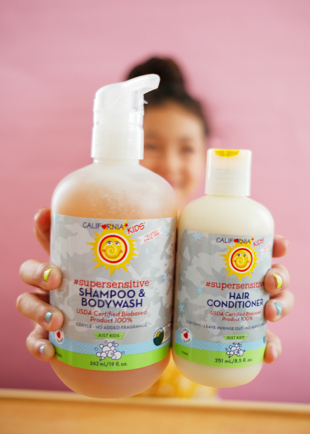 Kids super-sensitive shampoo and conditioner bottles held by a child