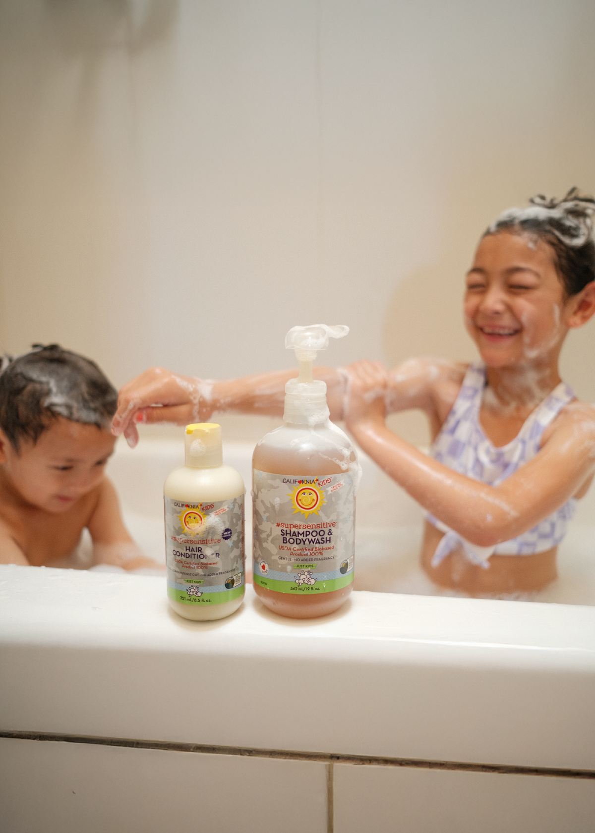 Kids super-sensitive body wash and shampoo bottles on bathroom sink with children washing