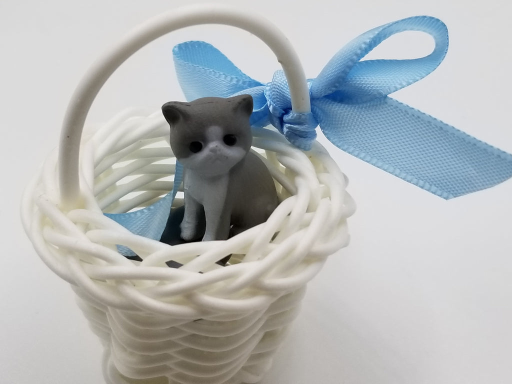 Small cat figurine in a white wicker basket with a blue ribbon bow