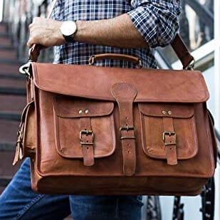 Leather briefcase held in hand with flap front and front buckle pockets in tan.