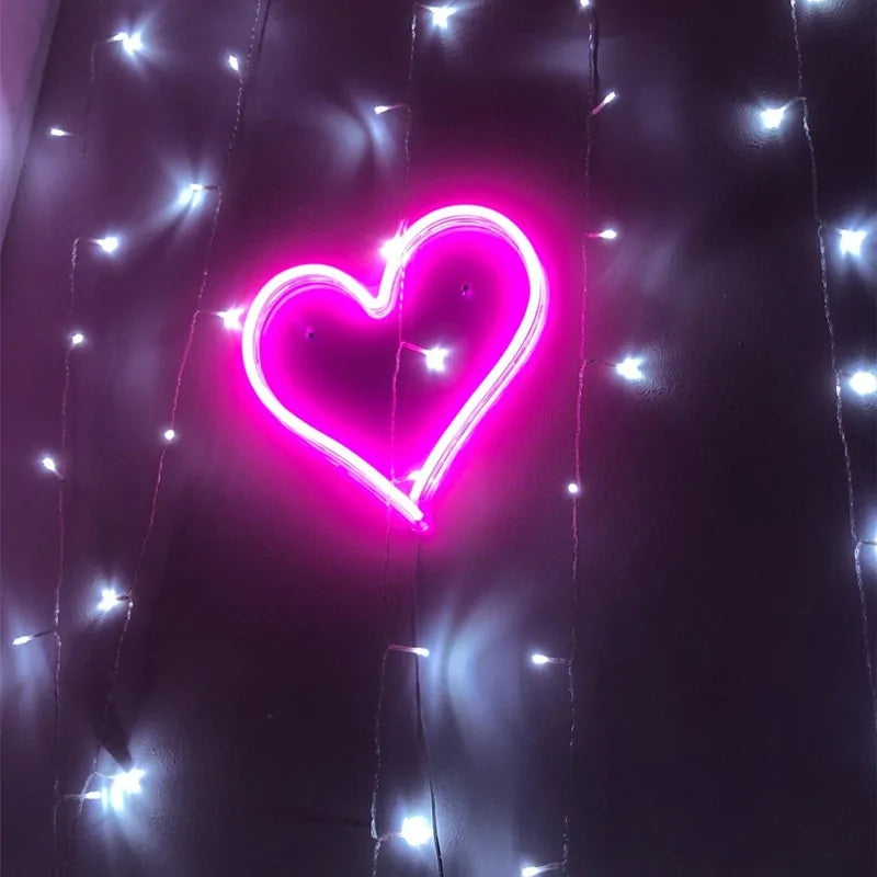 Pink heart neon LED wall sign glowing against dark backdrop with string lights