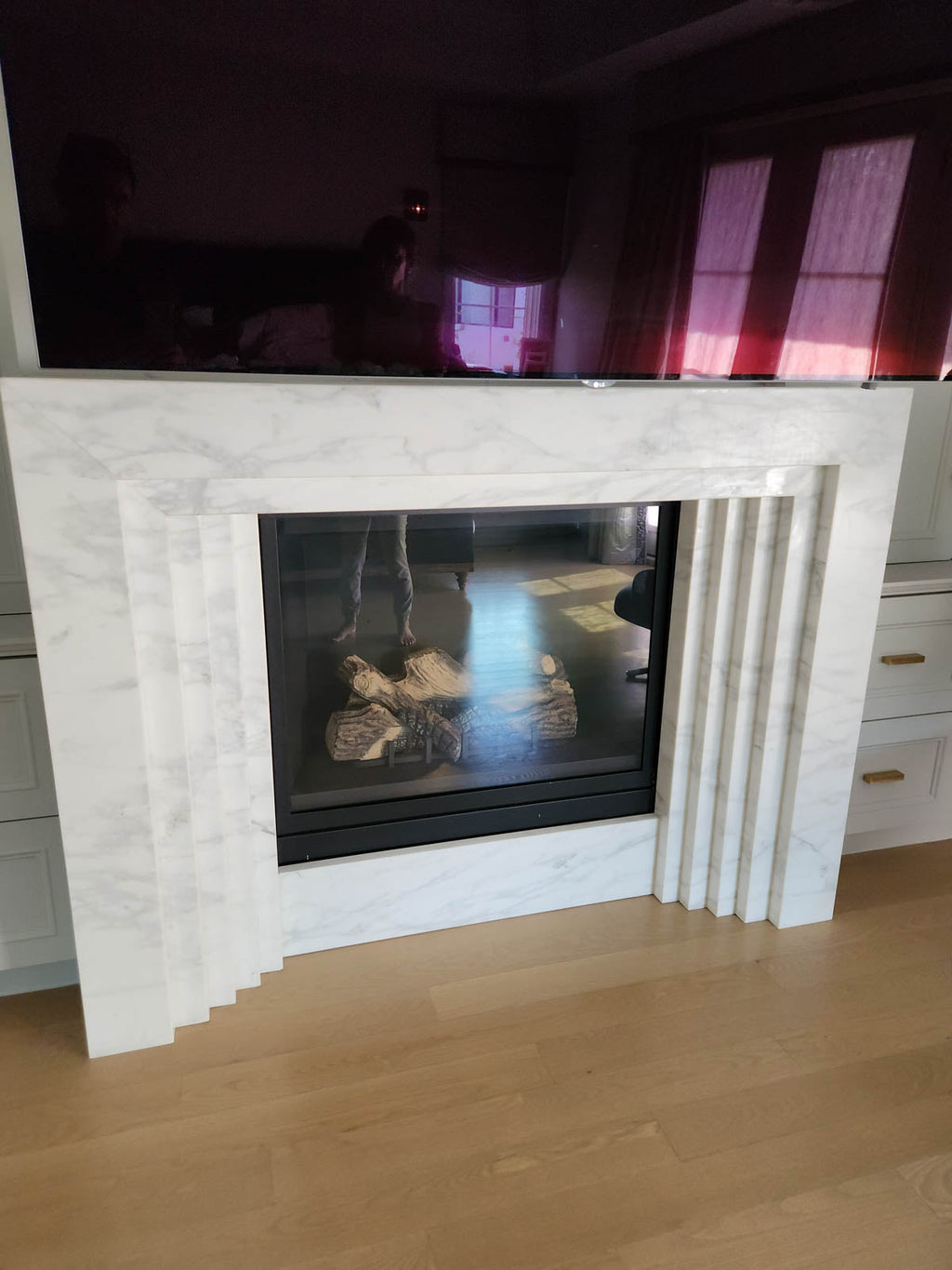 White marble fireplace surround with glass firebox opening and visible logs