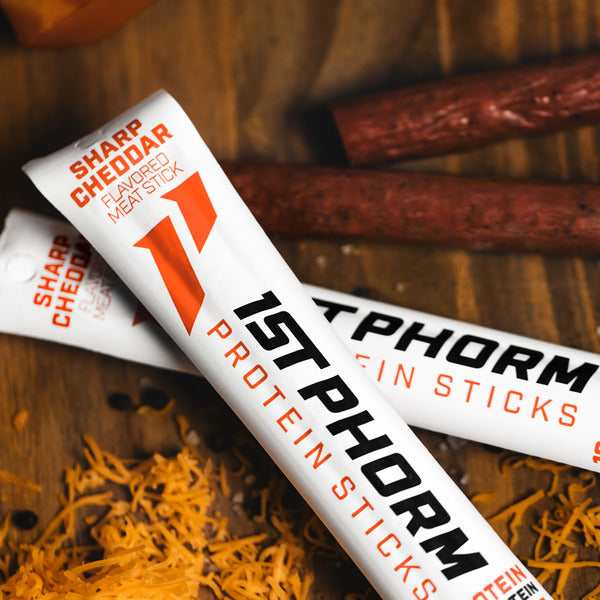 Sharp cheddar protein stick on white wrapper, angled view with large orange logo text