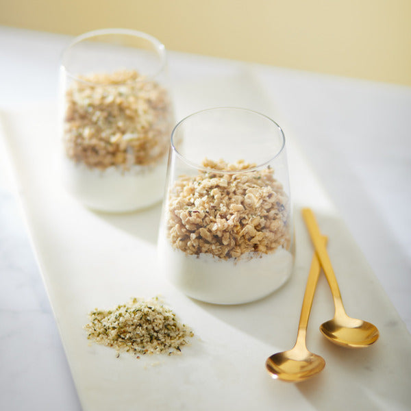 Granola in three white bowls with golden spoons on a tray