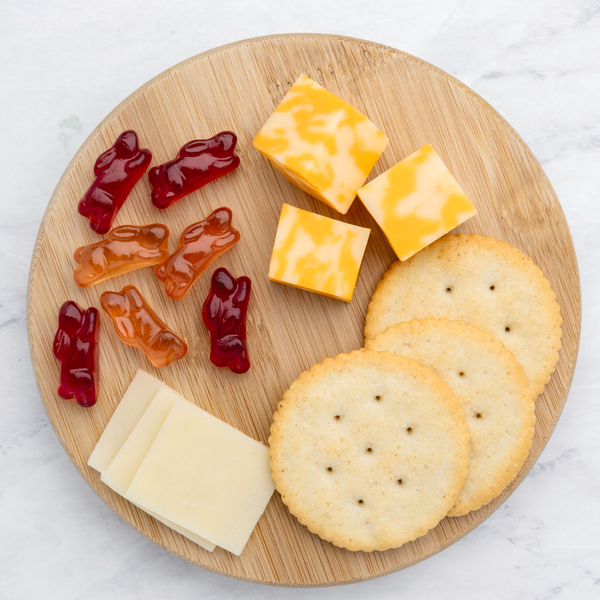 Fruit snack gummies and crackers with cheese on a round bamboo serving plate