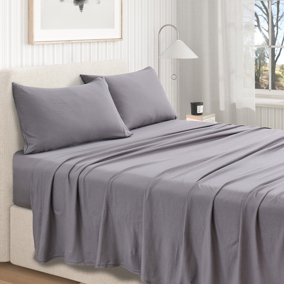 Grey jersey knit sheet set on bed with two pillowcases and flat sheet drape