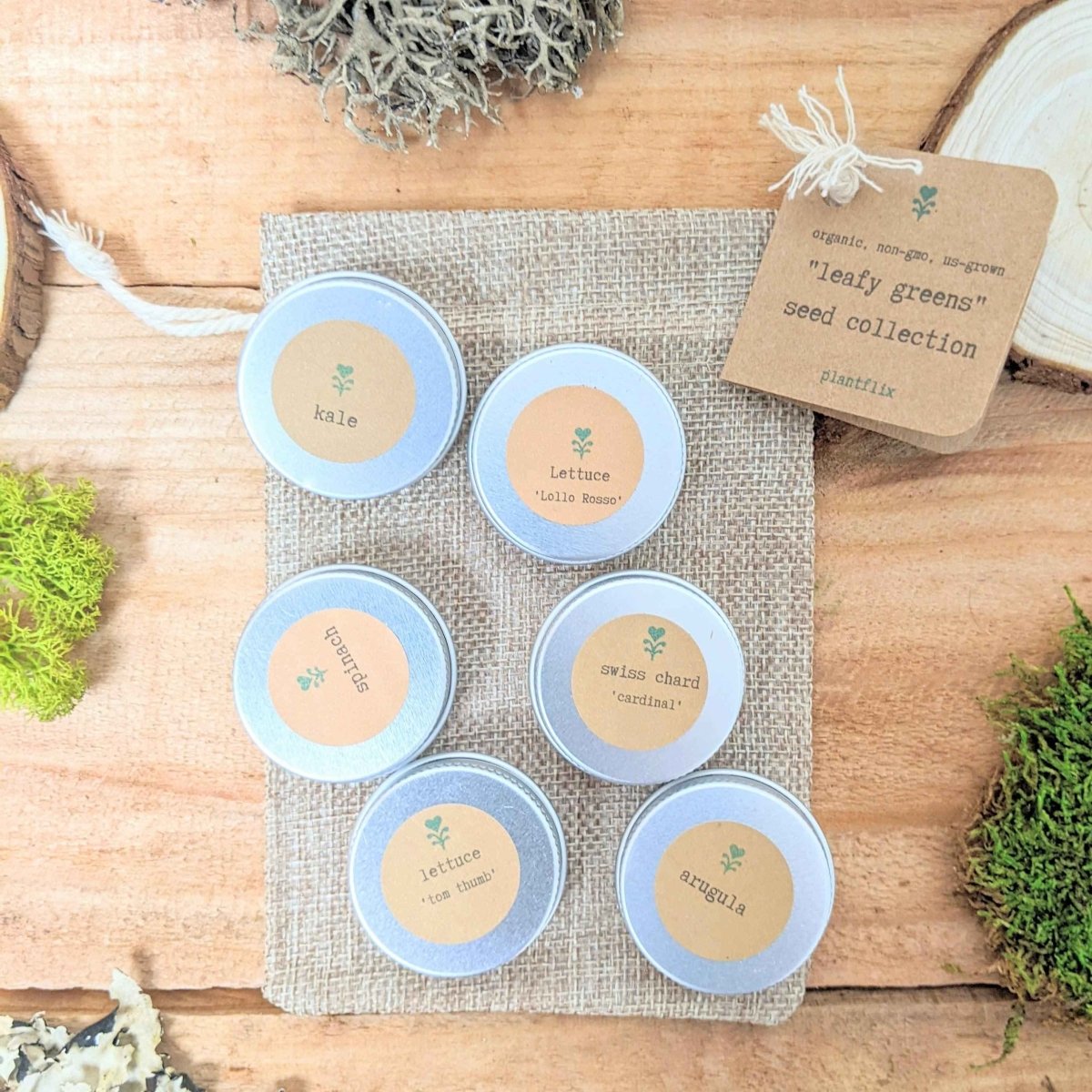 Leafy greens seed collection tins with printed variety labels on a burlap tray
