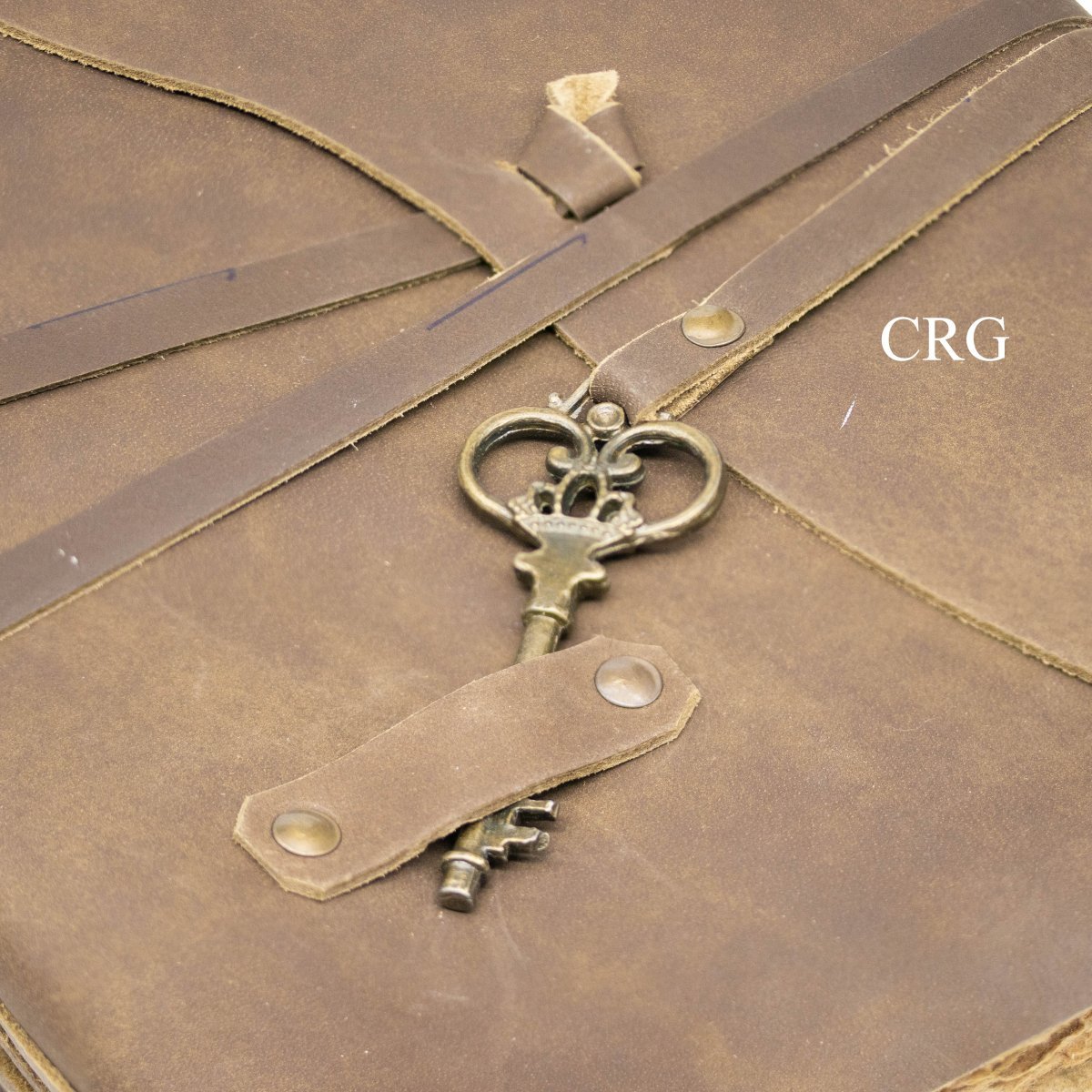 Leather journal detail: metal key charm with key on strap, brown.