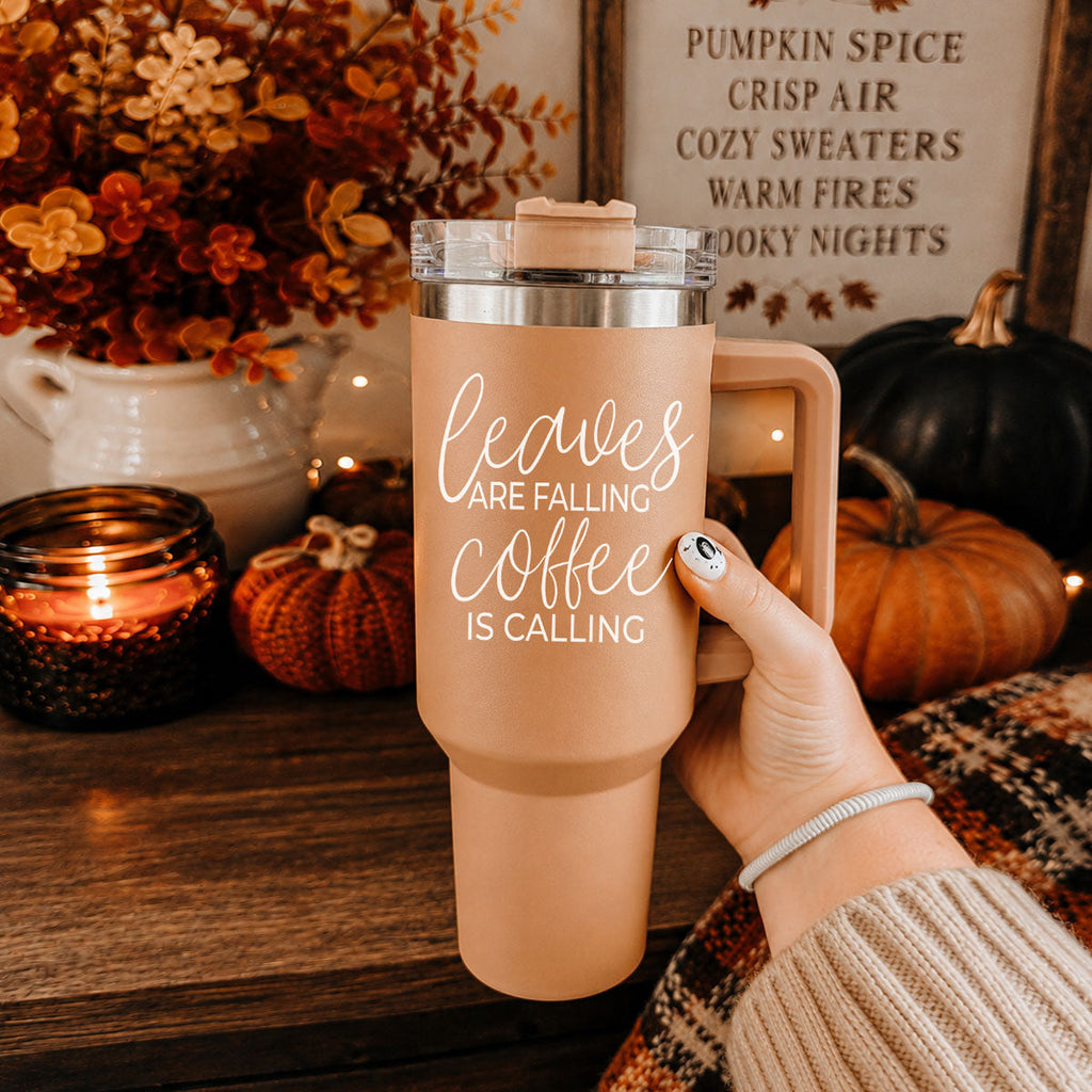 Taupe 40oz travel tumbler with clear lid and straw, rose handle, held by hand, “Leaves” text