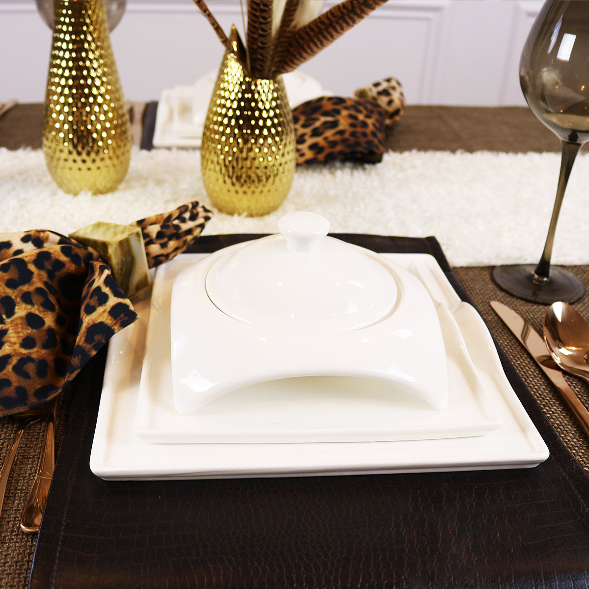 White porcelain covered serving dish on square tray with stacked plates