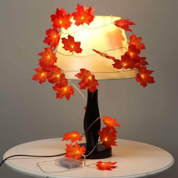 Lighted fall leaf LED string lights wrapped around a lamp base with glowing orange maple leaves