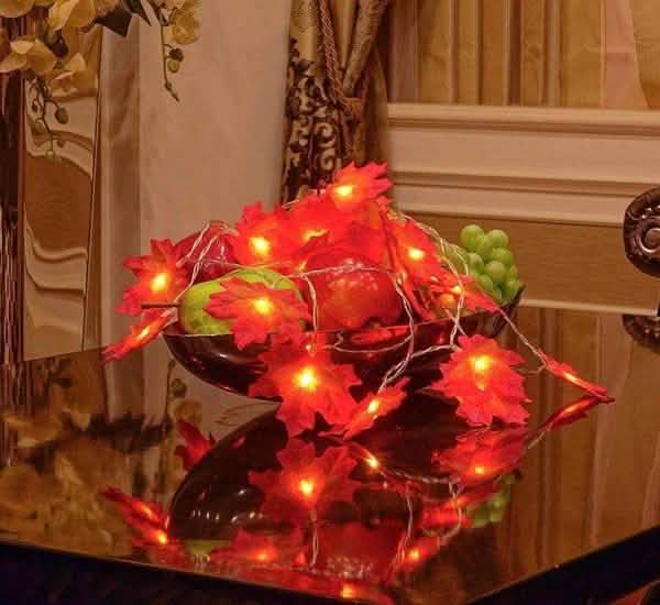 Lighted fall leaf LED string lights draped over a centerpiece with warm red-orange glow
