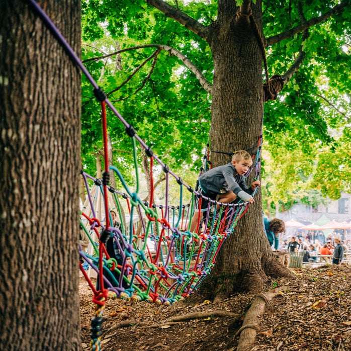 Rope suspension bridge attached to trees with multicolor net and cords