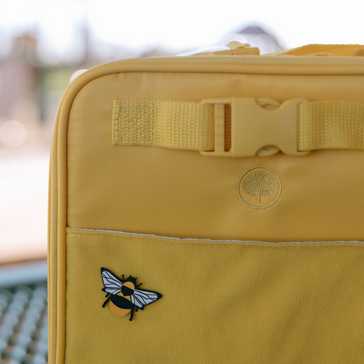 Yellow insulated lunch box close-up with belt strap and blue bee patch