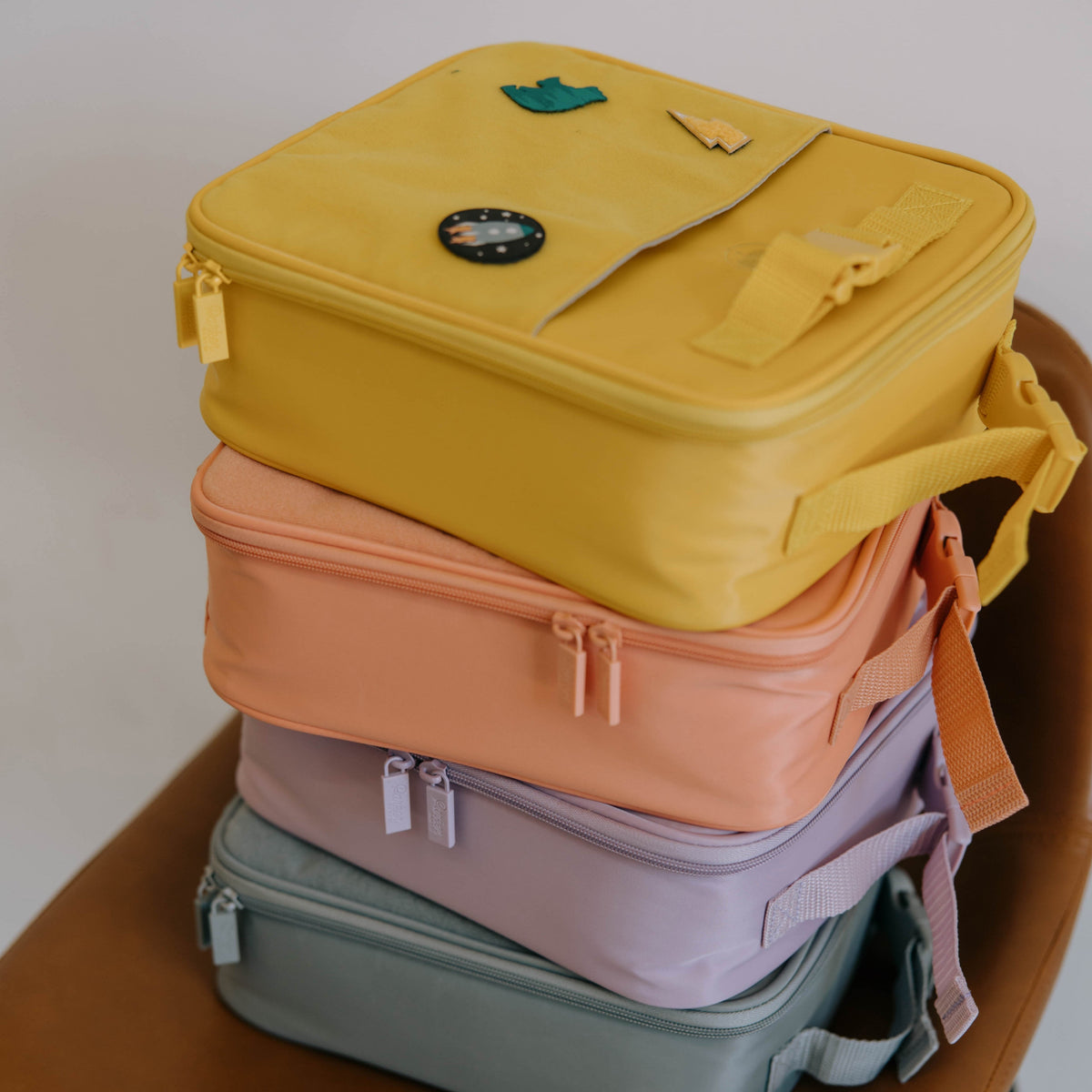Stacked insulated kids' lunch boxes in yellow, pink, lilac, and teal with handles