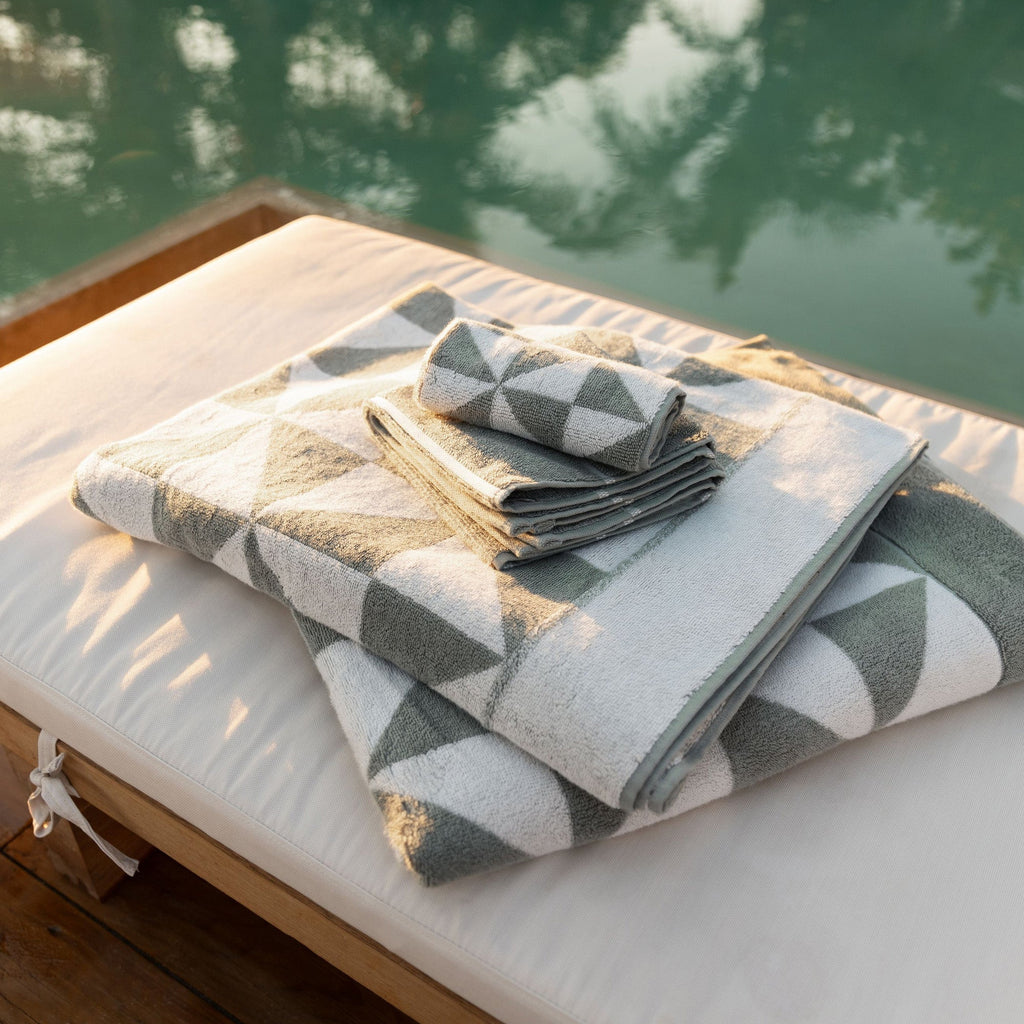 Folded sage green and ecru geometric cotton towels on a poolside lounge