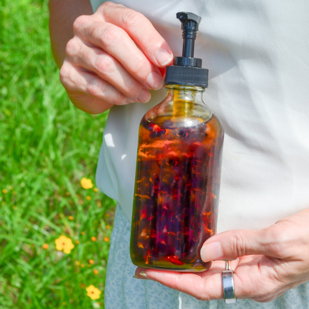 Amber body oil bottle with black pump held outdoors in green grass.