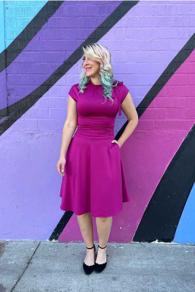 Magenta midi fitted dress with ruched waist, tied shoulder bow, and flared skirt