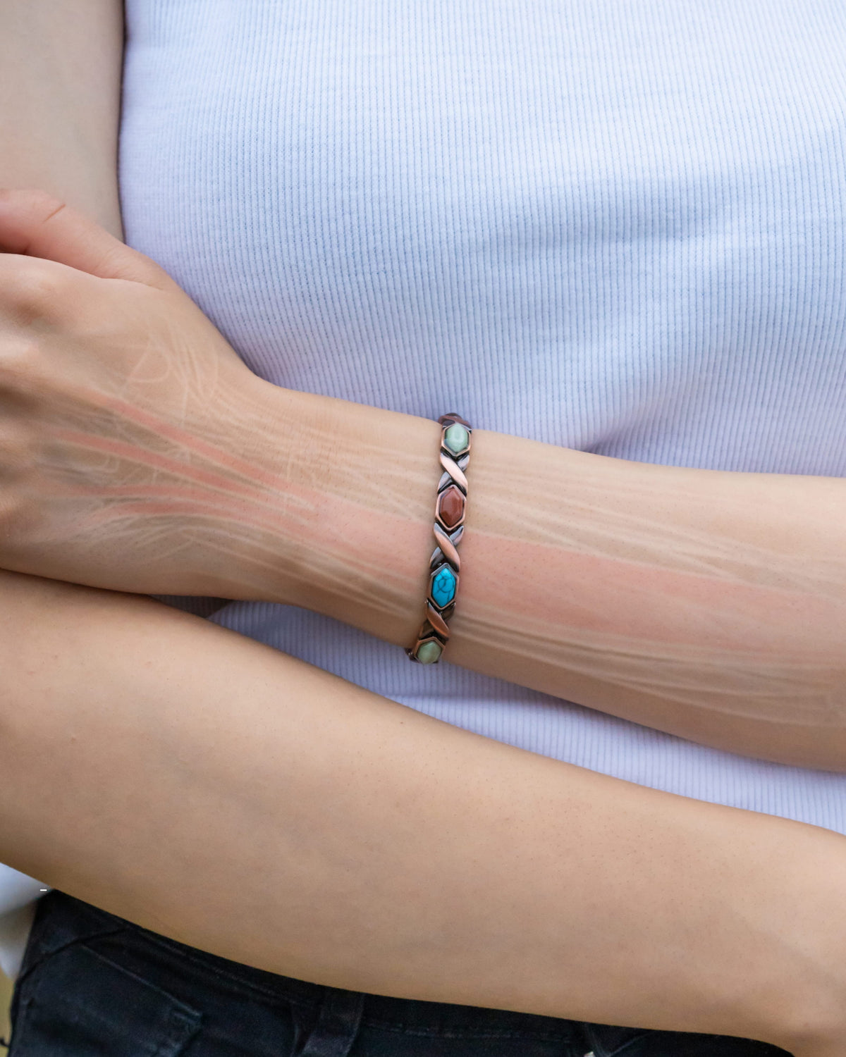 Copper magnetic bracelet on wrist with turquoise and dark stone link accents.