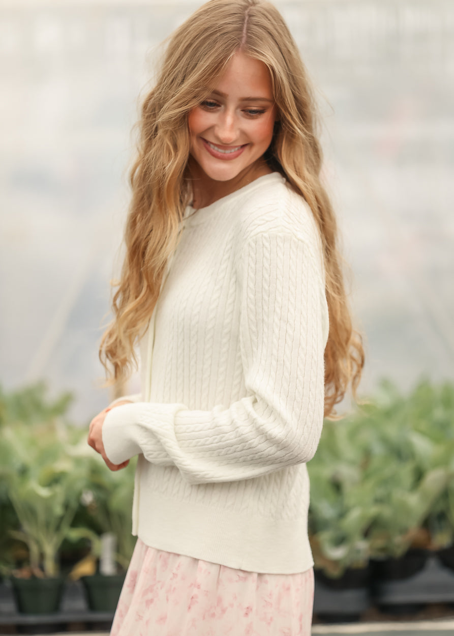 White cable-knit button cardigan with long sleeves and rounded neckline