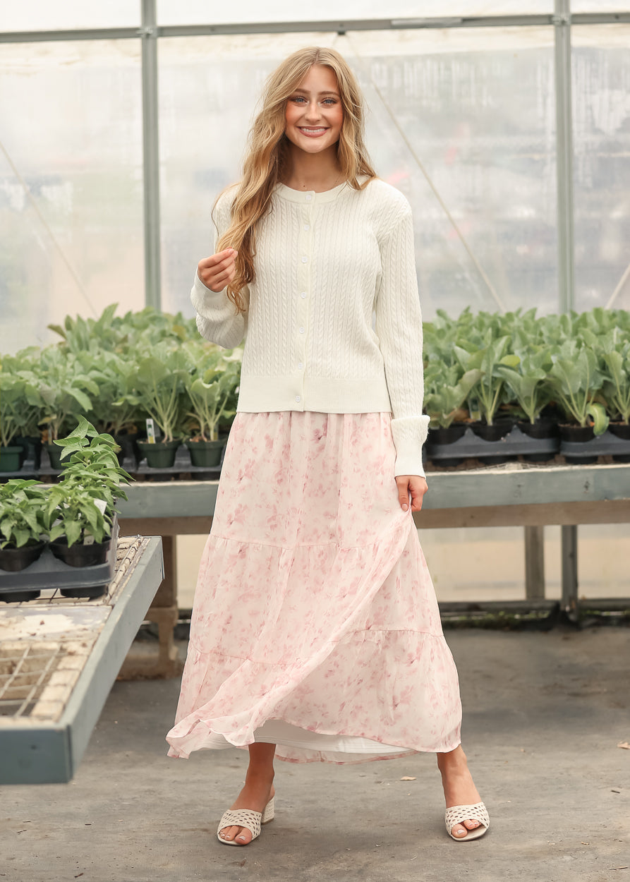 White button-up cardigan with cable texture, worn with a pink floral skirt
