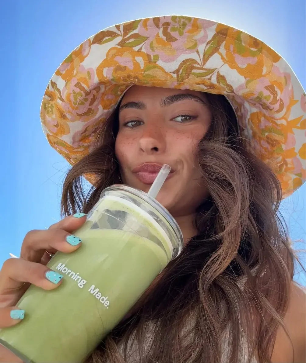 Woman sipping a green matcha latte from a cup with straw, holding can nearby