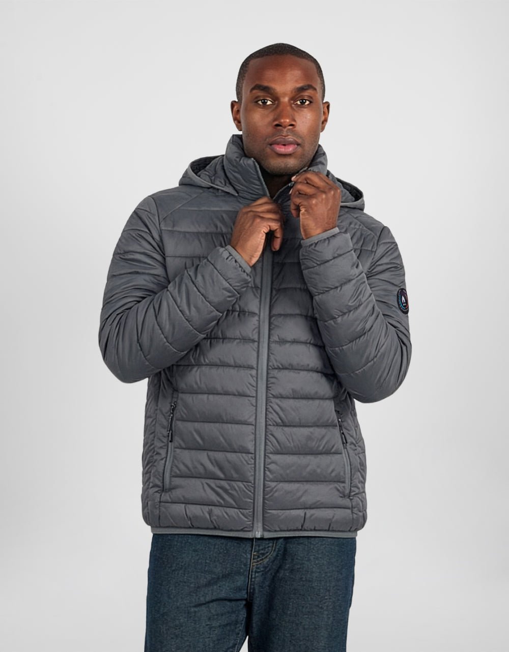 Men's gray hooded puffer jacket with full-zip front, quilted padding, sleeve patch.