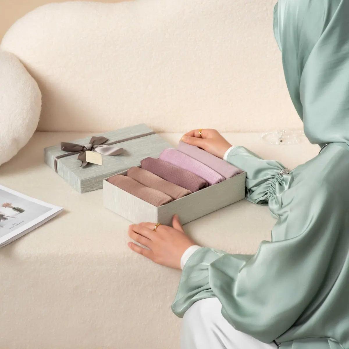 Textured hijab gift set box with lavender and mauve folds, hand placing scarf
