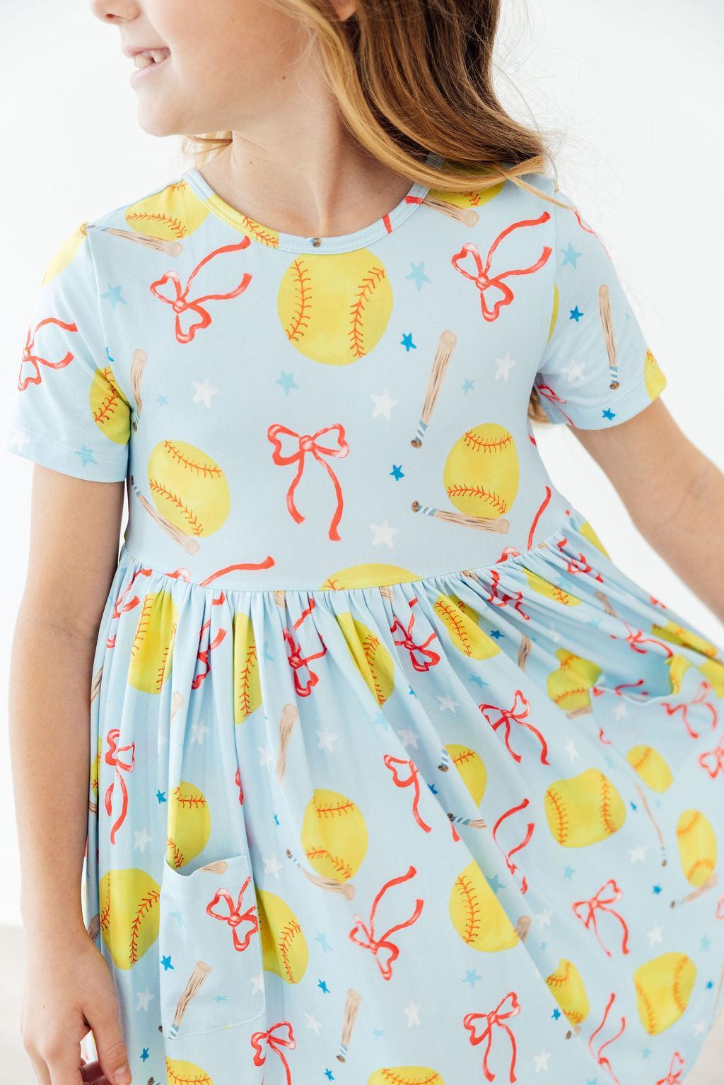 Light blue short-sleeve twirl dress with scattered softball, bow, and star prints