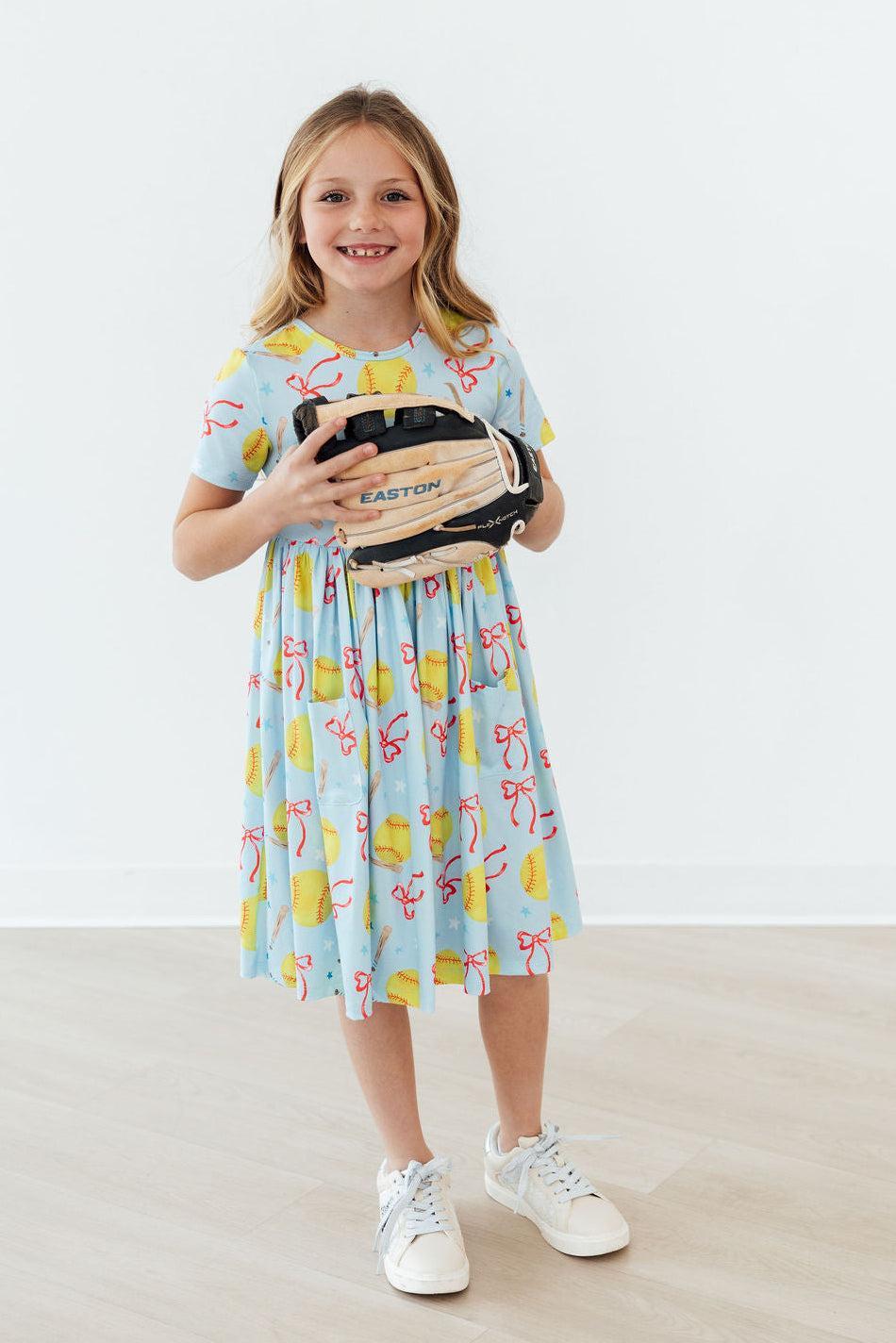Light blue short-sleeve twirl dress with colorful softball and bow graphics, sneakers