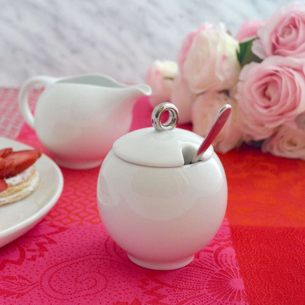 White ceramic sugar bowl with lid and creamer, with serving spoon resting inside